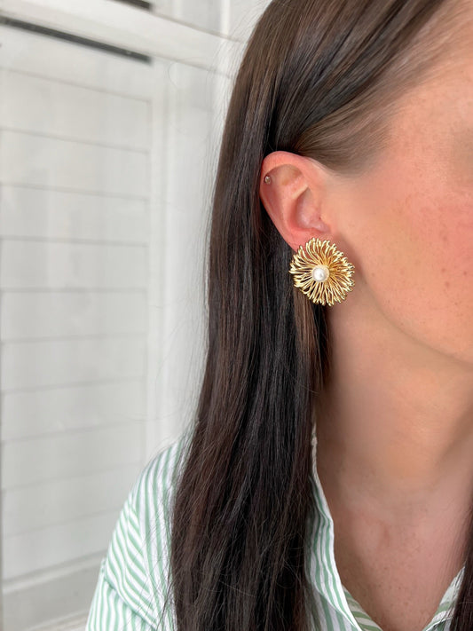 Gold earrings worn by a person with a neutral background